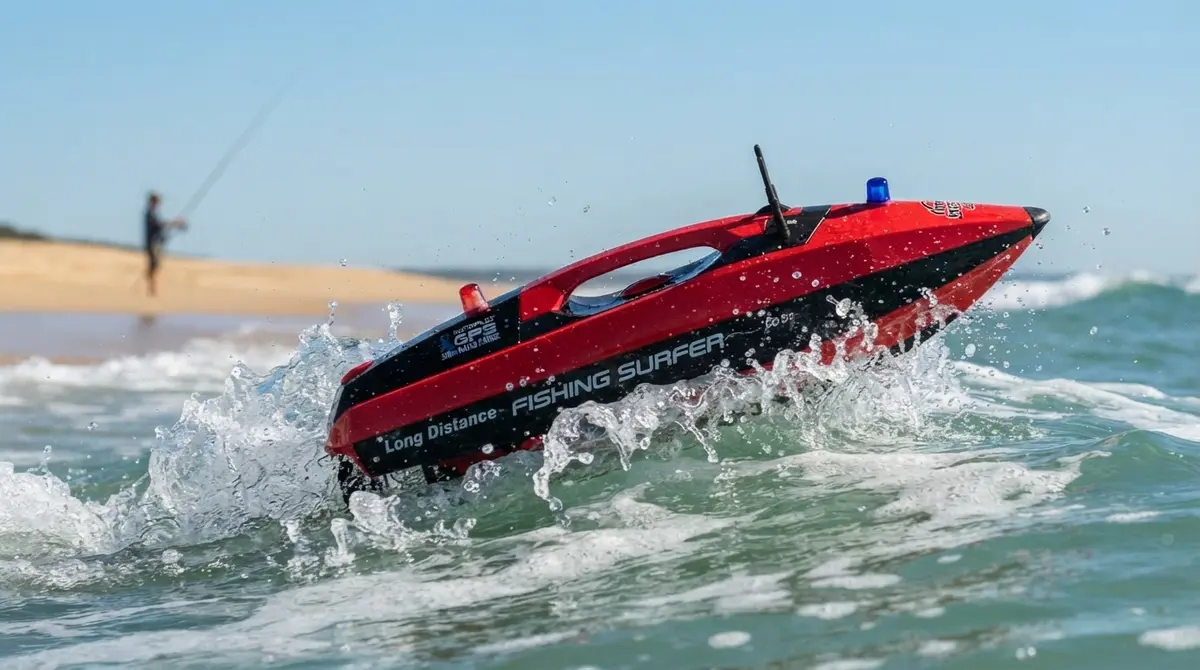 Red Joysway Fishing Surfer RC bait boat cutting through a breaking wave, with an angler surf fishing on the beach behind